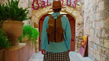 Şapkalı ve sırt çantalı bir kadın turist Mdina, Malta 'daki geleneksel dar sokaklar boyunca yürüyor..