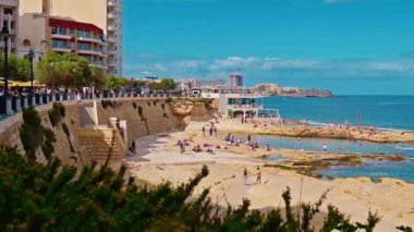 Sliema, Malta: Rocky plajları ve Sliema 'nın gezinti güvertesi. İnsanlar şehrin arka planında kayalık sahilde yüzüyor ve güneşleniyor..