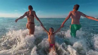 Bir anne ve genç oğlu, küçük kızlarını denizin yüzeyinde ellerinden tutuyorlar. Eğlenceli su oyunları. Denizde tatilde geçirilen eğlenceli zaman.