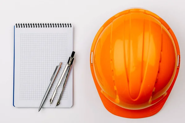 The view from the top with the orange helmet of the engineer under safety precautions and blank Notepad on a white background.