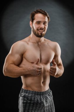 Tişörtsüz yakışıklı kaslı bir adam karanlık bir fotoğraf stüdyosunda fotoğrafçıya poz veriyor. Spor konsepti.
