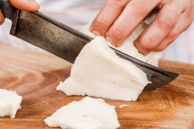 Aşçı çiğ domuz yağını tahta kesme tahtasıyla küçük parçalara ayırır.