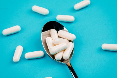 Tabletler mavi arka planda kaşığın etrafına rastgele dağılmış..