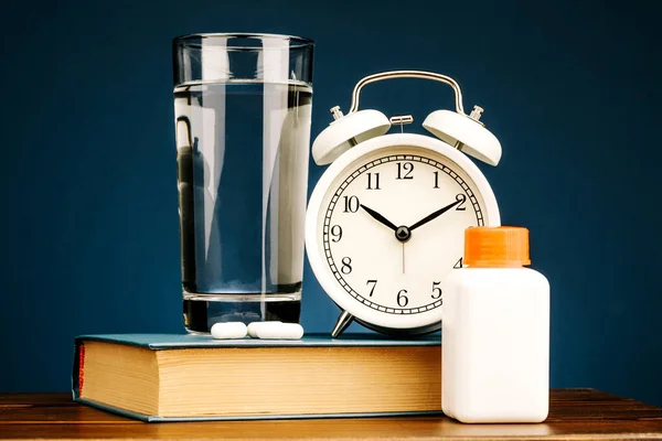 A mask, a glass of water, a book, pills, and an alarm clock. Restoring sleep patterns and treating insomnia.