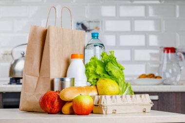 Eve güvenli teslimat. Mutfakta süt, meyve ve ekmek gibi çeşitli ürünlerin olduğu bir kutu..