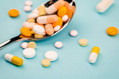 Tabletler mavi arka planda kaşığın etrafına rastgele dağılmış..