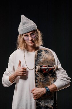 Stüdyoda kaykay tutan şık bir adamın portresi. Siyah arka planda poz veren gülümseyen bir kaykaycının yakın çekimi.