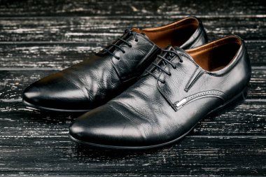 Ahşap bir masada siyah deri ayakkabılı erkek aksesuarları, sarı bir duvar arkasında bar ya da tezgah.