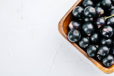 Beyaz beton bir masada, ahşap bir tahtanın üzerinde siyah frenk üzümü..