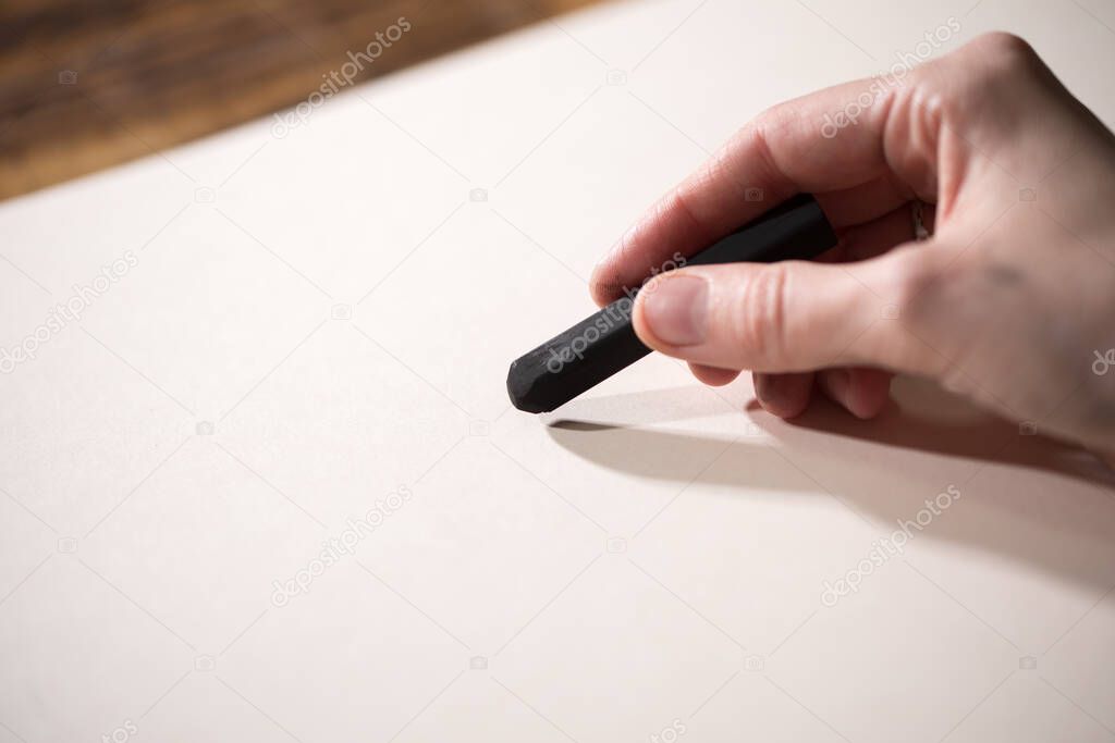 Close-up view of a painter on a white sheet. A man holds a pencil and draws.
