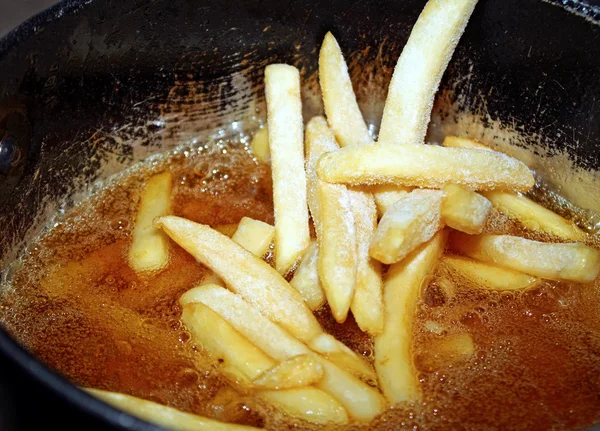 Замороженные картофель фри собирается в фритюрницу, наполненную горячим маслом — стоковое фото