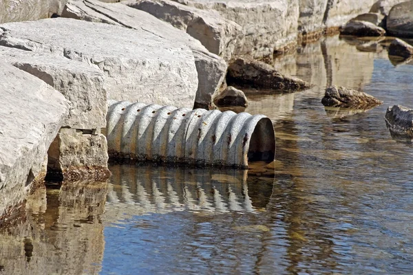 Large metal drain pipe leading out into natural lake — Stock fotografie