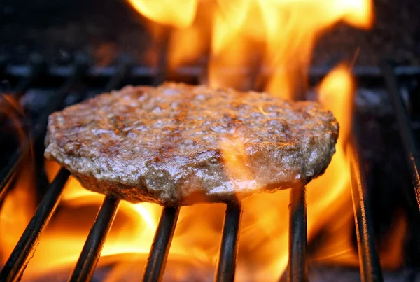 Juicy beef burger sizzling over hot flames on the barbecue — Stock Photo, Image