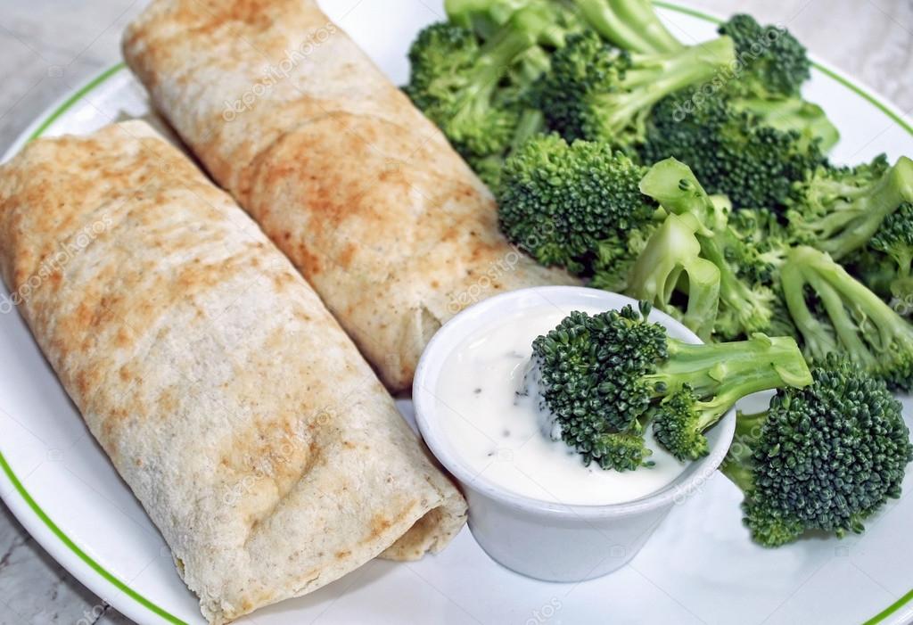 Two filled Tortilla wraps with a side of fresh raw broccoli and a container of creamy dressing for dipping