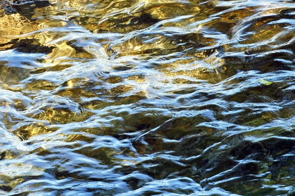 Sanft plätscherndes Wasser, das sich entlang des Flusses bewegt, mit sowohl Sonnenlicht als auch Schatten an der Oberfläche — Stockfoto