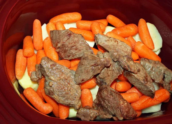 Layers of sliced white potatoes and carrots and browned stewing beef in a slow cooker — Stock Photo, Image