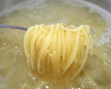 Cooked pasta noodles being lifted out of pot of boiling water with fork clipart