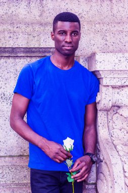 Genç Afrikalı Amerikalı adam New York 'ta seni özlüyor, mavi kısa kollu tişört giyiyor, kampüsün klasik duvarının köşesinde duruyor, elinde beyaz gül çiçeği tutuyor, ileriye bakıyor, bekliyor.