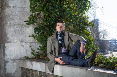 Genç bir adam büyük bir çerçevede oturuyor ve yabani yeşil bitkilerin önünde yukarı bakıyor ve derin derin düşünüyor.