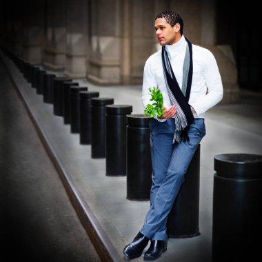 Yakışıklı genç bir adam bir demet yeşil yaprak tutuyor, kışın eski caddede duruyor, bekliyor ve düşünüyor. Umut kavramı ve ruh hali. Güzel bir sanat rengi fotoğrafçılığı.