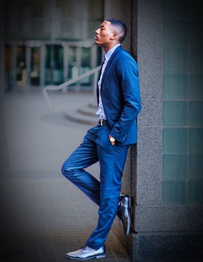 Duvara yaslanmış genç, yakışıklı, siyah bir adam dışarıda derin bir şekilde düşünüyor. Güzel bir sanat yaşam tarzı fotoğrafı.