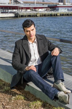 Genç bir işadamı nehir kenarında oturuyor ve derin derin düşünüyor.