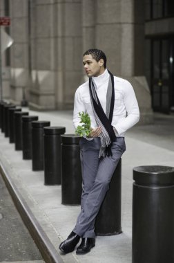 Genç adam bir demet yeşil bitki tutuyor, dışarıda bekliyor, düşünüyor, umut ediyor, diliyor.