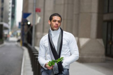 Genç adam bir demet yeşil bitki tutuyor, dışarıda bekliyor, düşünüyor, umut ediyor, diliyor.