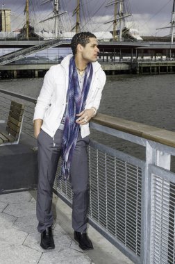 Genç yakışıklı bir adam nehrin çitlerinin yanında duruyor, uzaklara bakıyor.