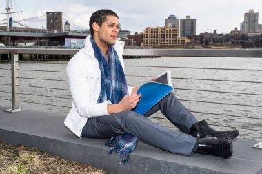 Genç ve yakışıklı bir öğrenci nehir kenarında oturuyor, kitap okuyor ve düşünüyor.