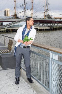 Bir demet yeşil yaprak tutarken, genç ve yakışıklı bir adam nehrin çitlerinde dikiliyor, uzaklara bakıyor..