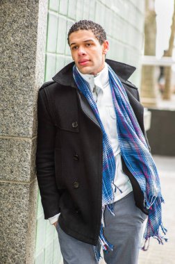 Duvara yaslanmış genç ve yakışıklı bir adam başka tarafa bakıyor ve düşünüyor.