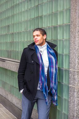 Yeşil bir duvara güvenerek, genç yakışıklı bir adam başka tarafa bakıyor ve düşünüyor.