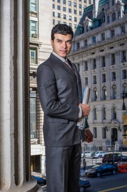 Genç bir işadamı bir ofis binasının önünde belgeleri tutuyor ve savaş arıyor.