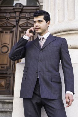 Genç bir işadamı bir ofis binasının önünde duruyor ve telefonla konuşuyor.