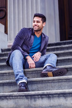 Genç adam dışarıda dinleniyor. Koyu mor yün ceket, mavi kot pantolon ve siyah deri ayakkabılar giyen genç bir Orta Doğulu, dışarıda merdivenlerde oturmuş etrafa bakıyor ve gülümsüyor.