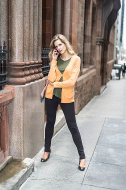 Elinde bir dergi, dışarıda bir sokakta genç ve güzel bir kadın bir telefon görüşmesi yapıyor. 