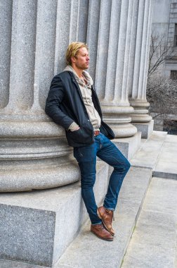 Dışarıda siyah bir ceket, içeride kapüşonlu bir ceket, kot pantolon ve çizme giymiş genç yakışıklı bir adam bir sütuna yaslanıyor ve şöyle düşünüyor:.