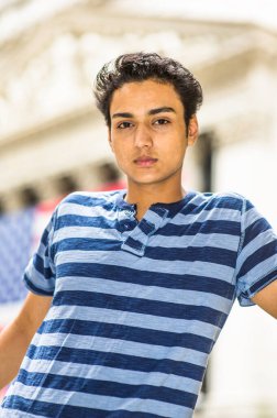 Mavi çizgili tişört giyen Asyalı bir genç düşünceli bir şekilde sana bakıyor..
