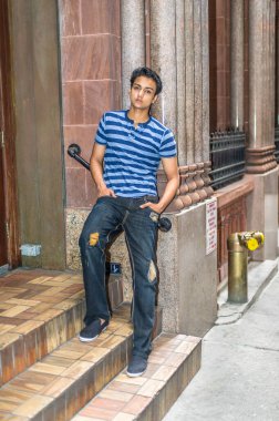 Bir atlet, şık bir pantolon giymiş genç Asyalı bir genç kapı eşiğine dayanıyor ve derin düşüncelere dalıyor..