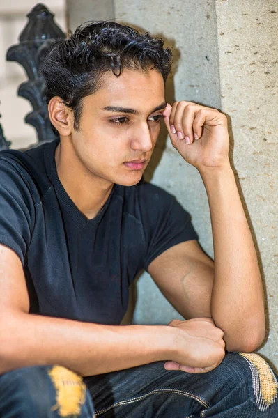 Siyah tişörtü ve şık pantolonu olan, bir sütuna yaslanan ve siyah metal korkulukların yanında duran genç ve çekici Asyalı bir genç dışarıda mola veriyor.