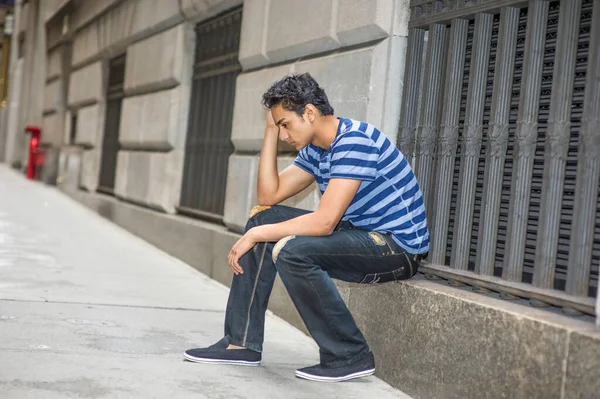 Mavi çizgili bir tişört, şık bir pantolon giymiş, genç Asyalı bir genç bir pencerede oturuyor, kafasını kaşıyarak düşünüyor.