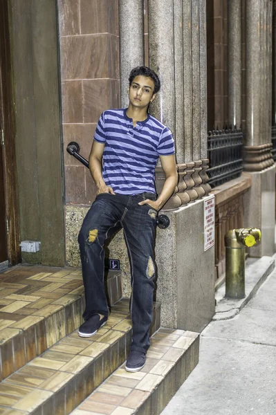 Bir atlet, şık bir pantolon giymiş genç Asyalı bir genç kapı eşiğine dayanıyor ve derin düşüncelere dalıyor..