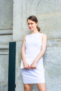 Beyaz kolsuz iş kıyafetleri giymiş, elinde küçük bir bilgisayar olan bir iş kadını, dışarıda durmuş, büyüleyici bir şekilde sana bakıyor.