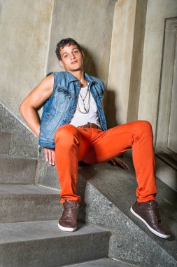 Dışarıda ve duvarın önünde oturan genç bir adam sana bakıyor.