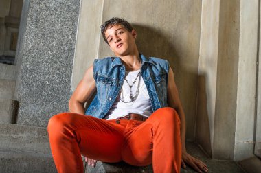 Dışarıda ve duvarın önünde oturan genç bir adam sana bakıyor.