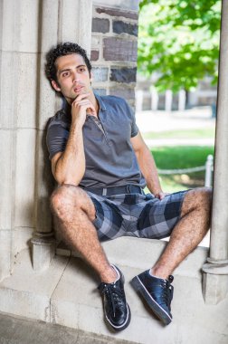 Gri gömlekli, şortlu, siyah deri ayakkabılı, bir eli çenesine değen genç, güçlü yakışıklı bir adam eski moda bir pencerede oturuyor ve derin düşüncelere dalıyor..