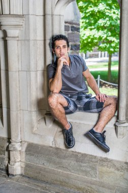 Gri gömlekli, şortlu, siyah deri ayakkabılı, bir eli çenesine değen genç, güçlü, yakışıklı bir adam eski moda bir pencerede oturuyor ve sana bakıyor..
