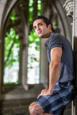 Genç yakışıklı bir adam kemer penceresinin yanında duruyor ve ileriye bakıyor..