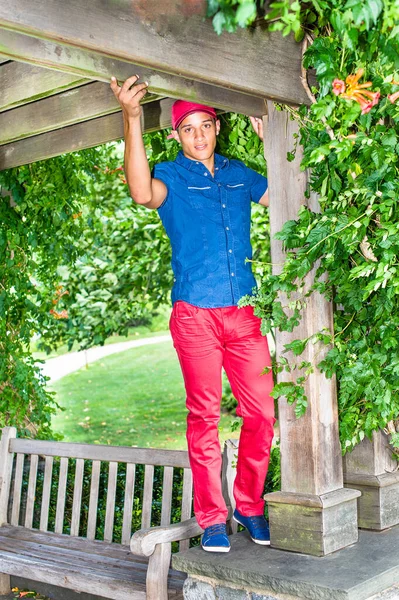 Dressing in a red baseball hat, blue short sleeve shirt,  red pants and blue shoes, a handsome, attractive guy is playing around in the park.
